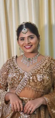 Smiling bride in a gold lehenga with an emerald necklace